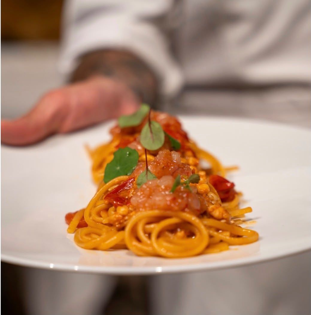 Spaghetti al pomodoro con basilico serviti su un piatto bianco, tenuto in mano da una persona sullo sfondo