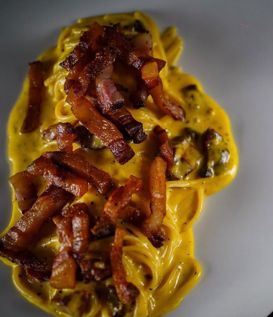 Pasta condita con una cremosa salsa gialla e pezzetti di pancetta croccante su un piatto bianco