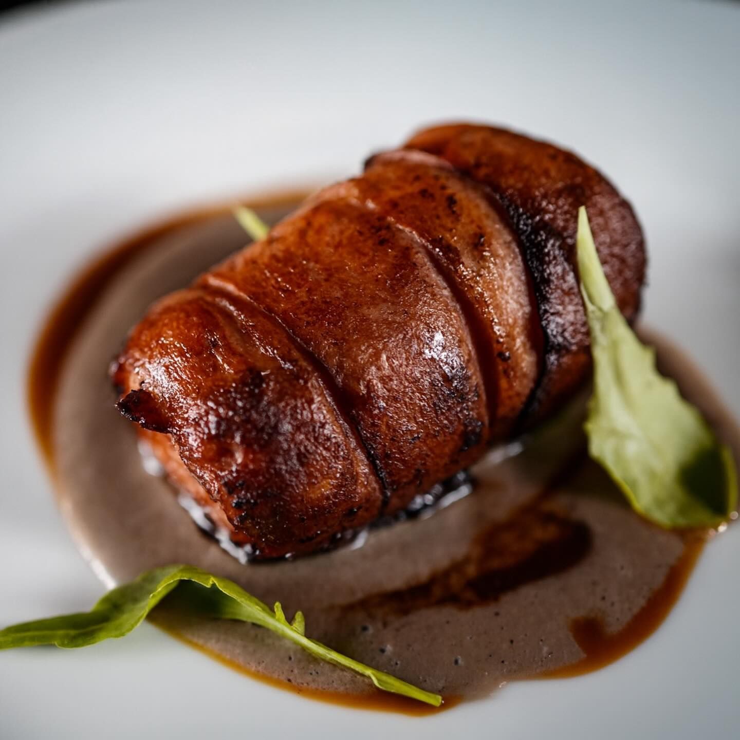 Arrosto glassato arrotolato su un piatto bianco, con salsa scura e foglie verdi