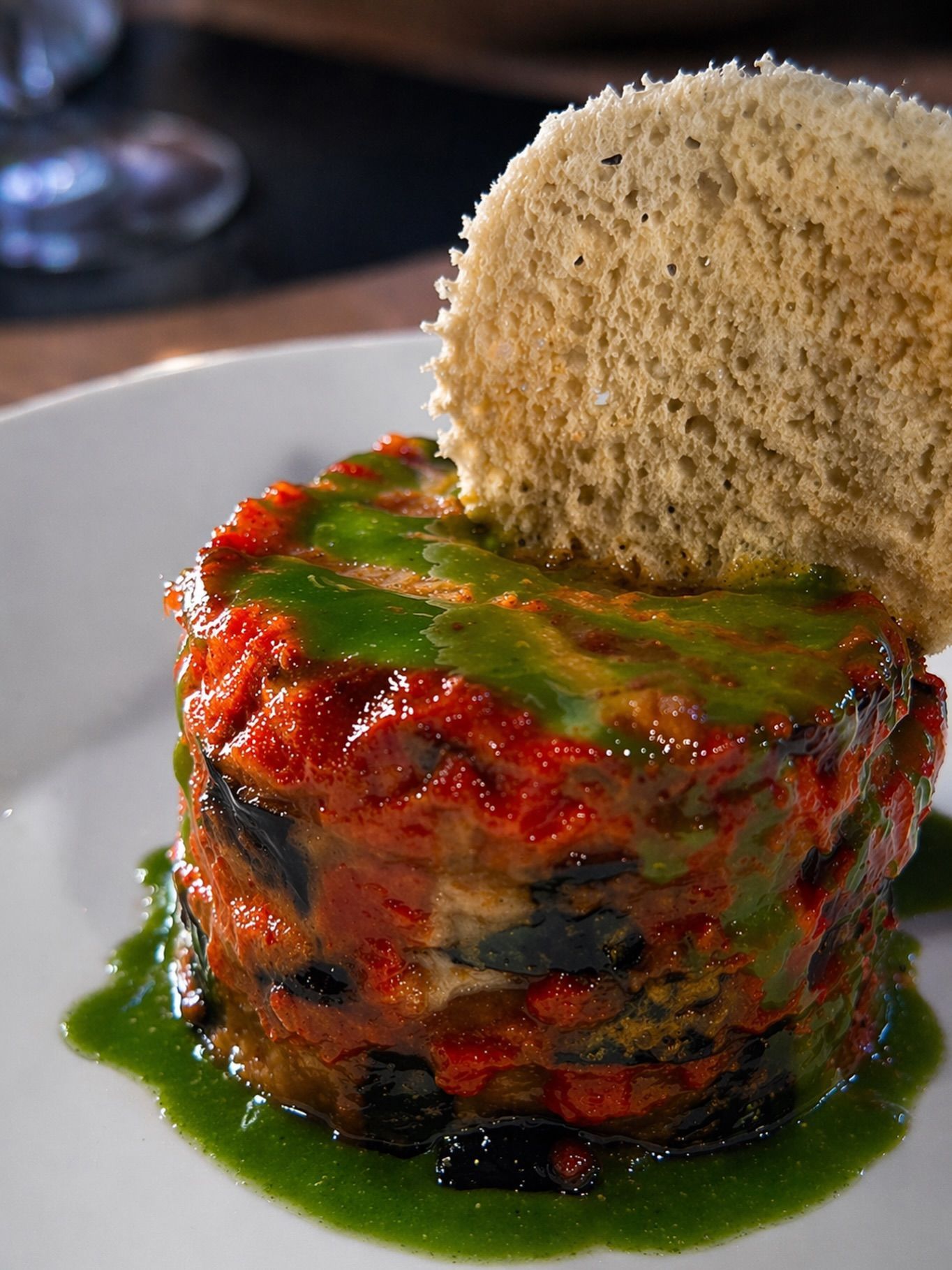 Piatto stratificato con salsa rossa e olio verde, guarnito con una cialda croccante di pane, su un piatto bianco