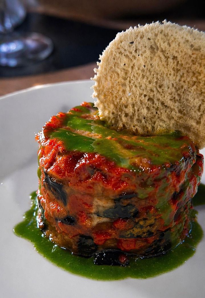 Piatto gourmet di verdure a strati con salsa verde e una cialda rotonda croccante, servito su un piatto bianco