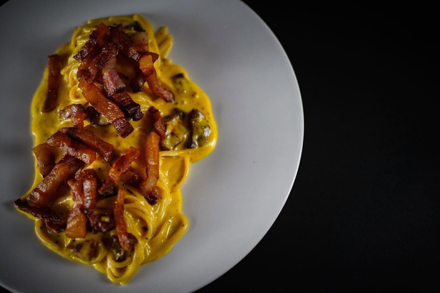 Piatto di pasta con salsa gialla cremosa e pancetta croccante su sfondo scuro