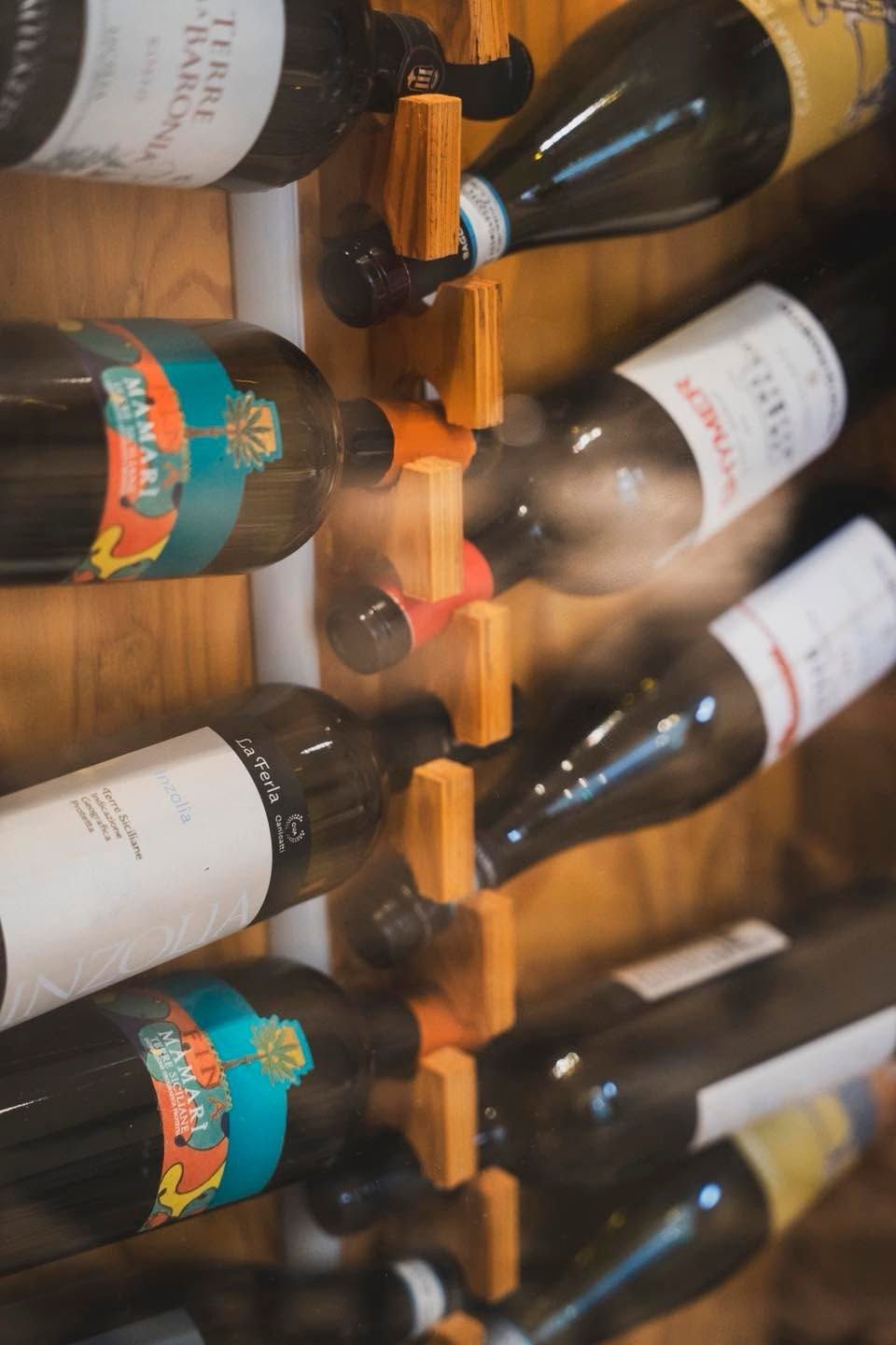 Bottiglie di vino impilate su scaffali di legno in una cantina, con le etichette rivolte verso l’esterno