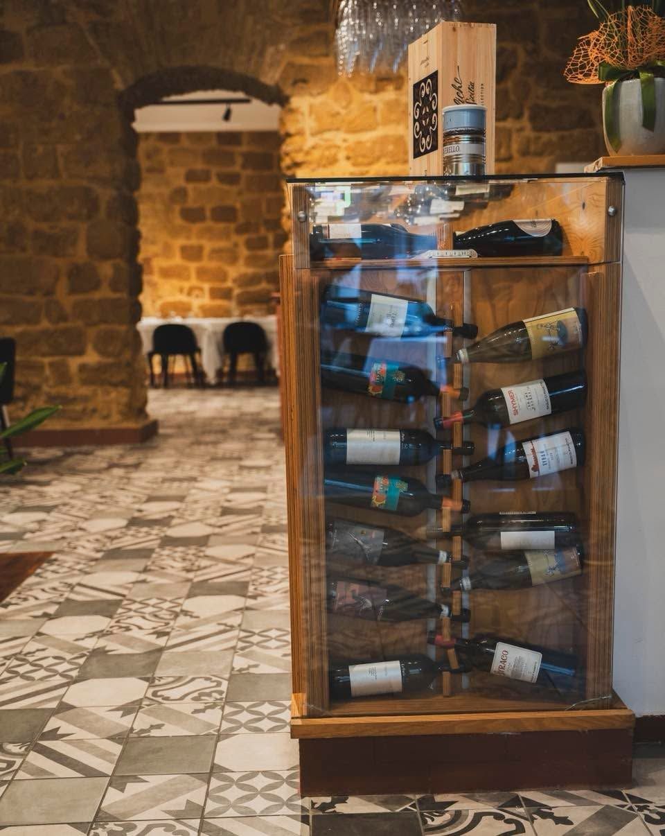 Bottiglie di vino esposte in una credenza con ante in vetro, in una rustica cantina in pietra o nel corridoio di un ristorante.