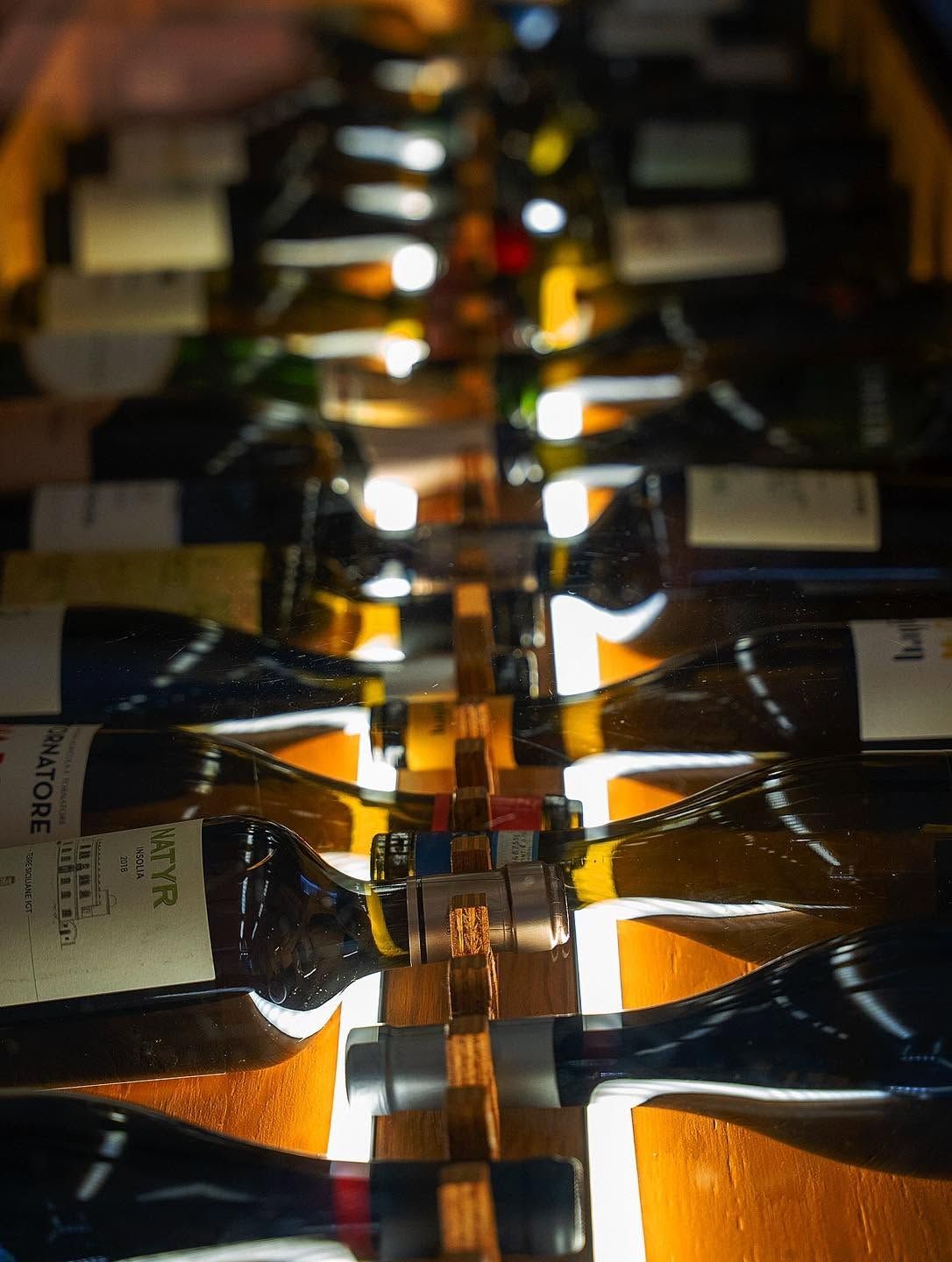 File di bottiglie di vino allineate in una cantina, illuminate da una calda luce arancione