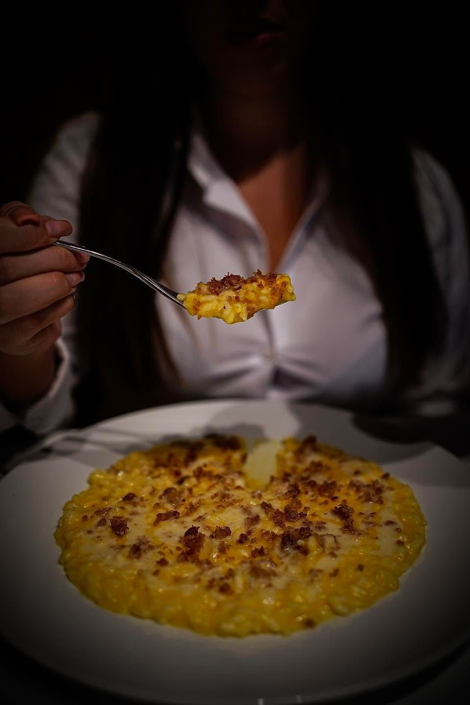 Una persona tiene in mano un cucchiaio colmo di riso giallo sopra un piatto di riso, in un ambiente poco illuminato