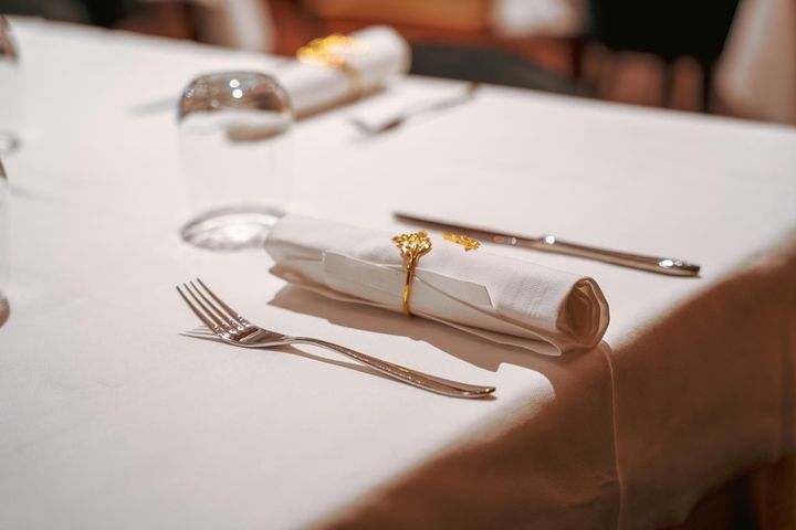 Elegante mise en place con un tovagliolo bianco piegato, un portatovagliolo dorato, posate e un calice da vino