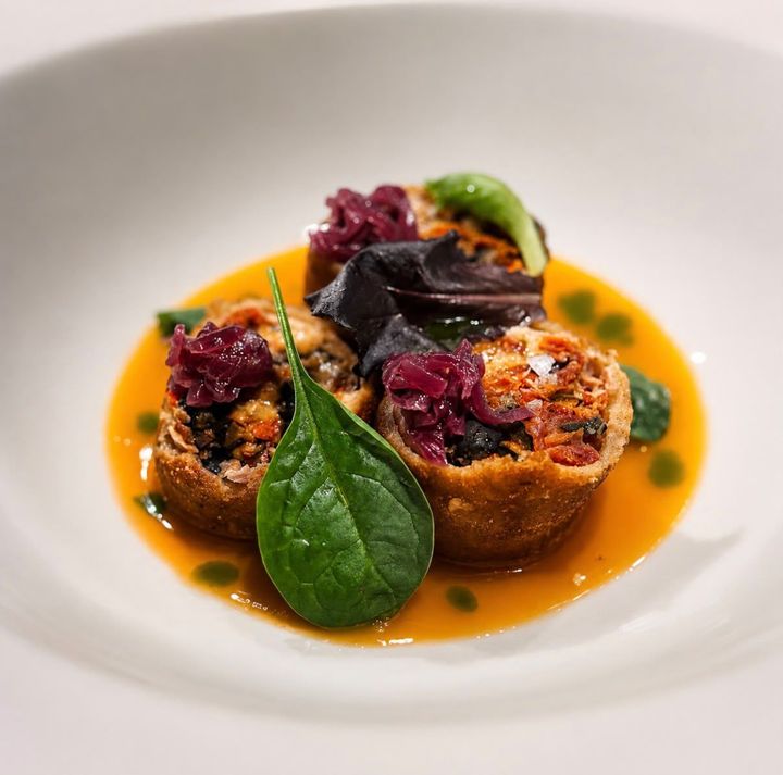 Antipasto gourmet impiattato con salsa all’arancia, fagottino ripieno e microgreens su un piatto bianco