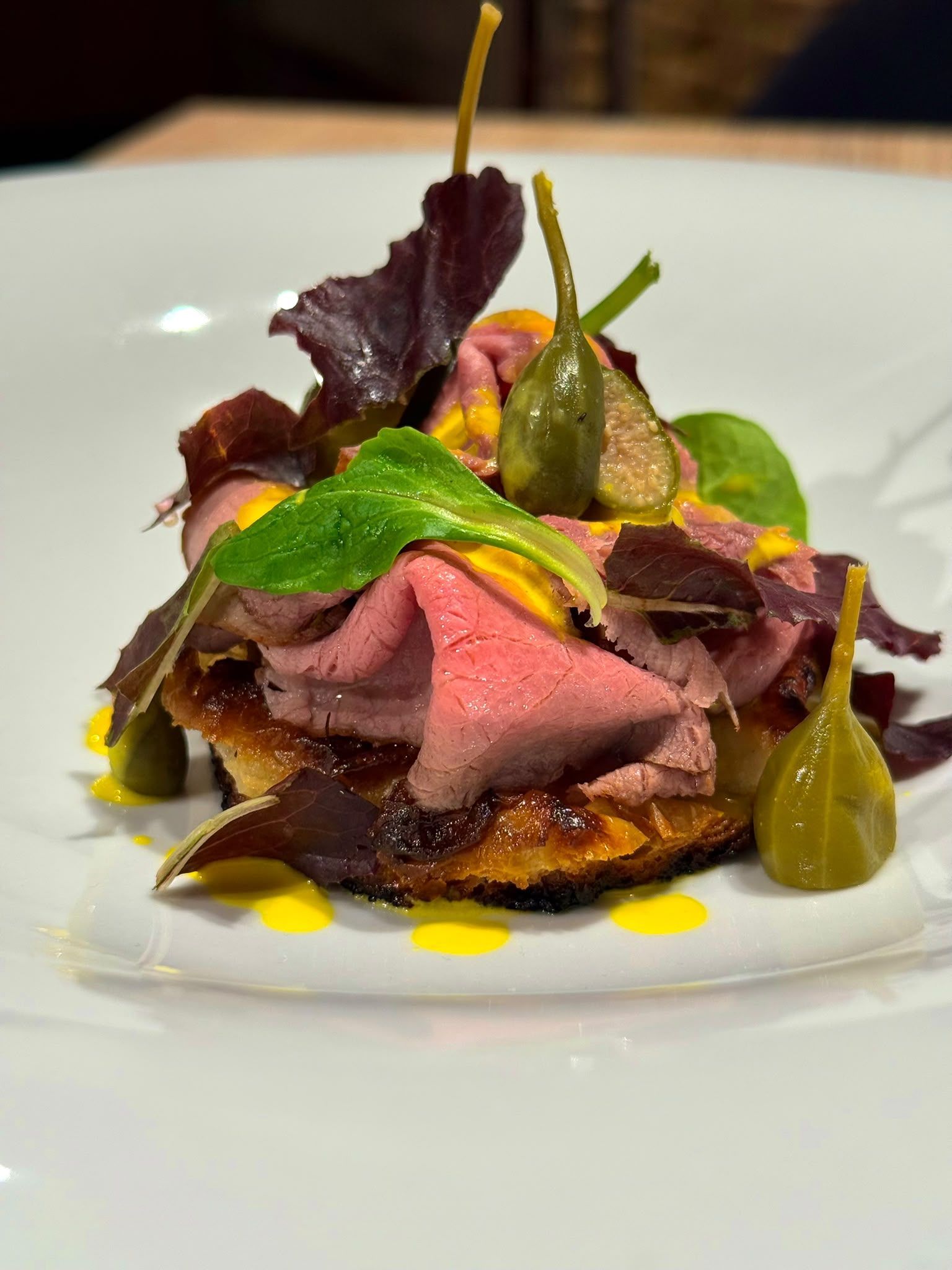Piatto gourmet di carne impiattato con verdure e salsa, guarnito con erbe aromatiche su un piatto bianco
