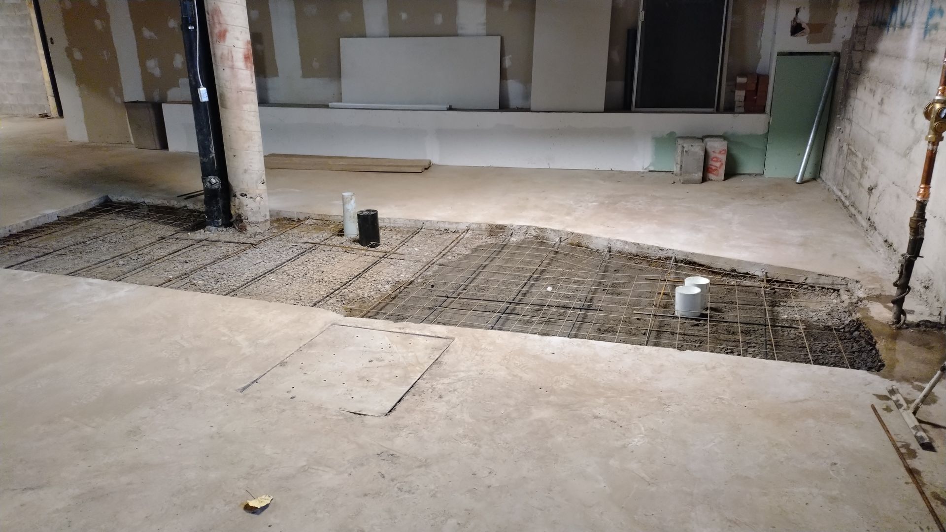 Sous-sol en construction ; béton apparent, plomberie et armatures métalliques.