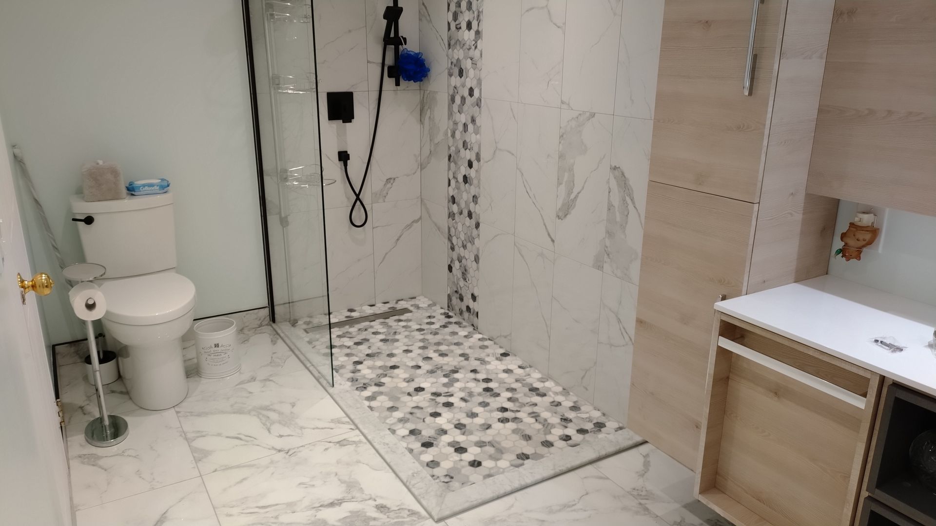 Salle de bains avec carrelage imitation marbre, douche en verre avec sol en galets et toilettes.