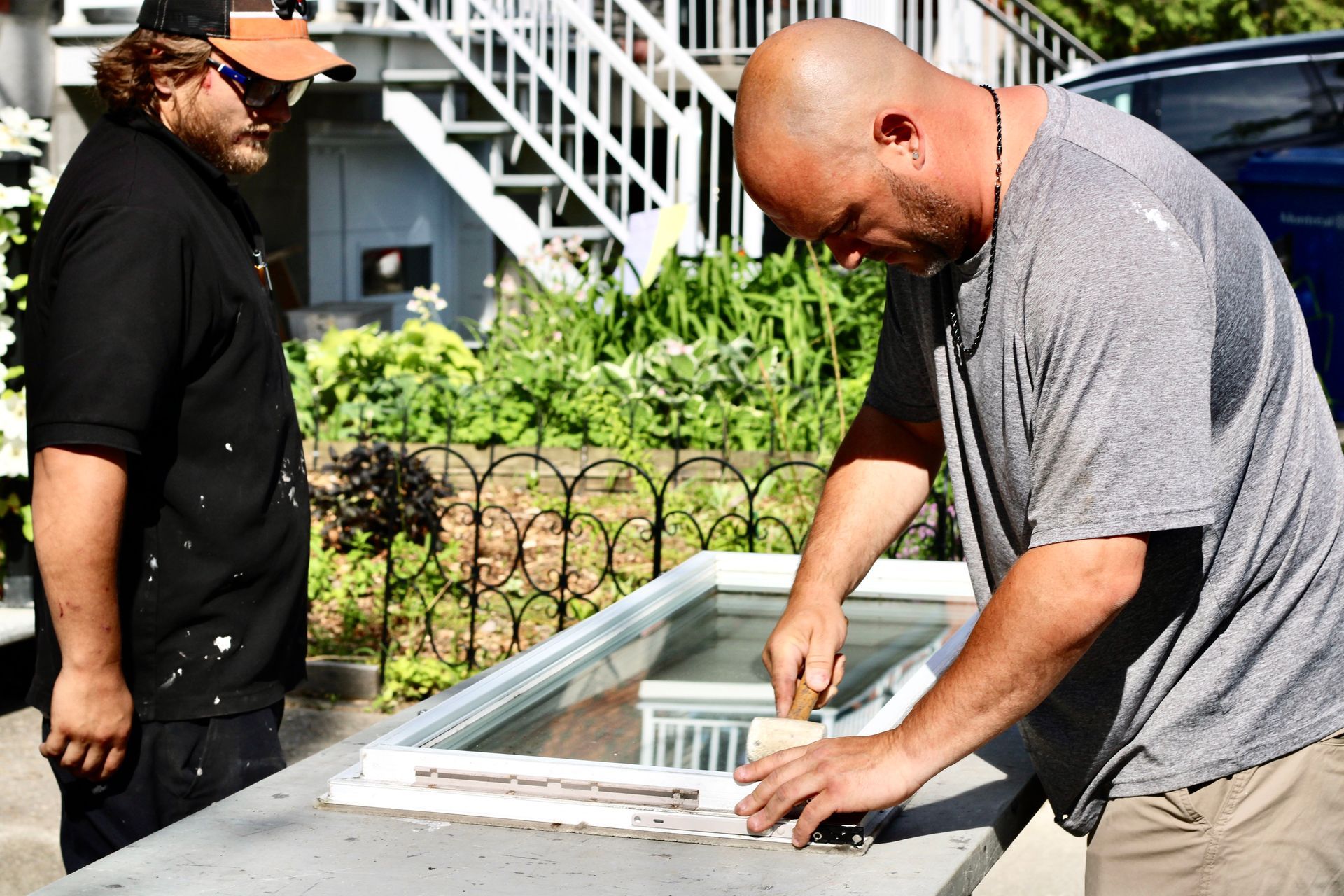 Deux hommes inspectent un enclos extérieur vitré, situé à côté d'un escalier et de verdure.
