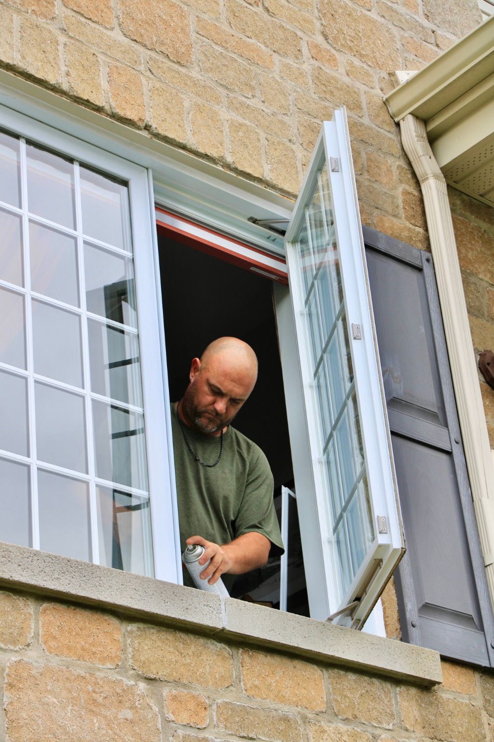 Man standing in an open window, adjusting a white blind on a brick building