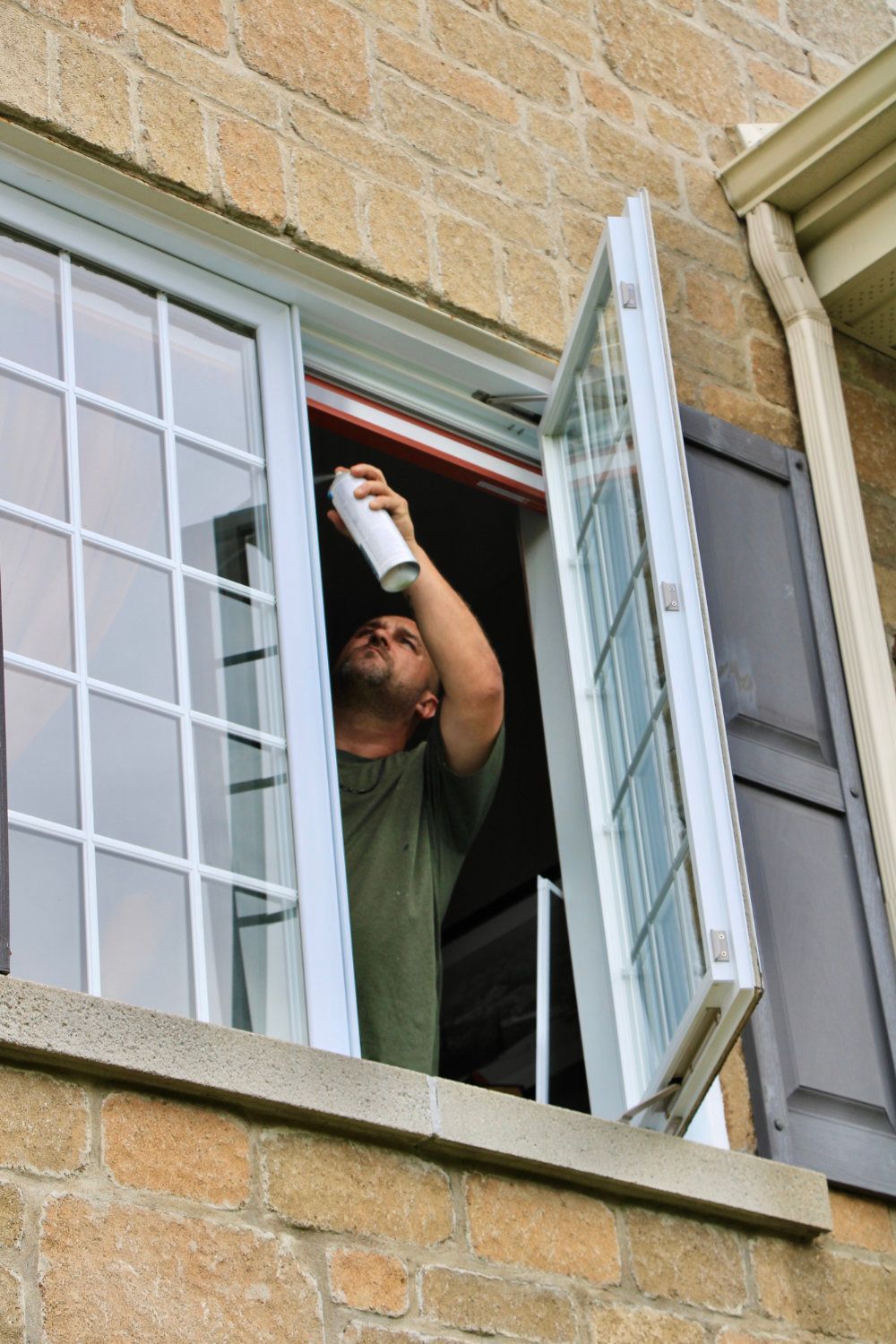 Person spraying a can into an open window from inside a brick building