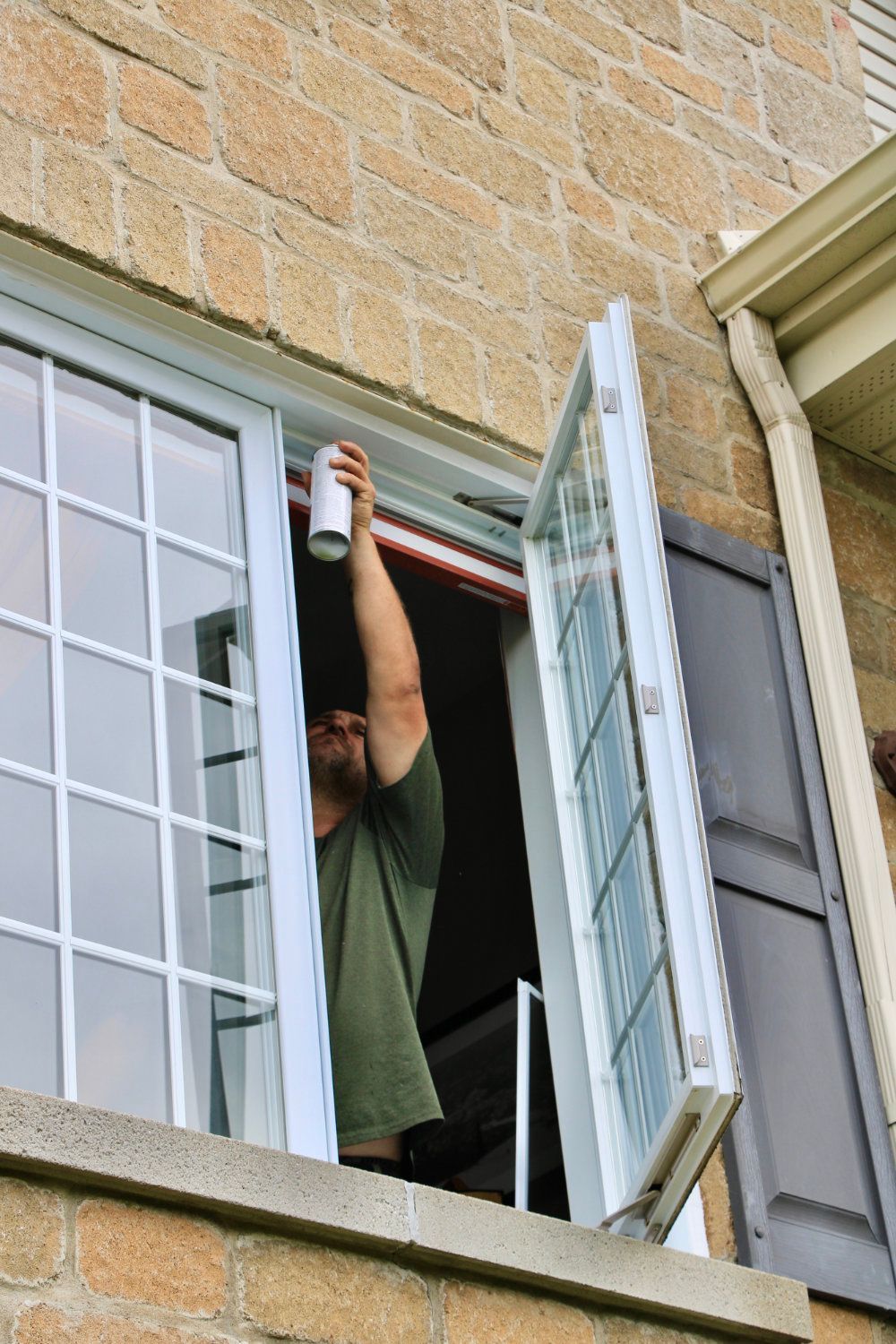 Person spraying cleaner on an open window from inside a brick building