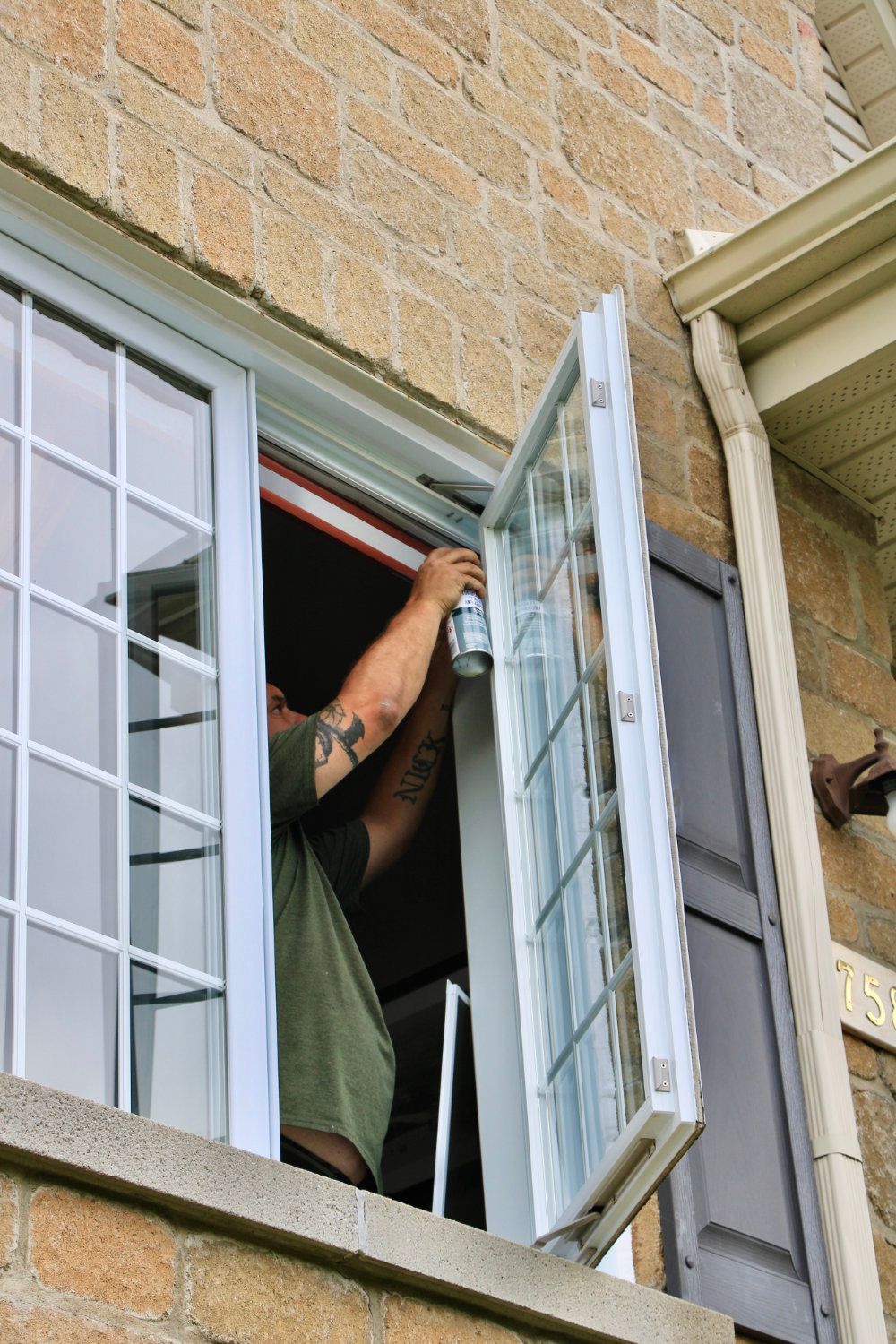 Person opening a white shuttered window from inside a brick building
