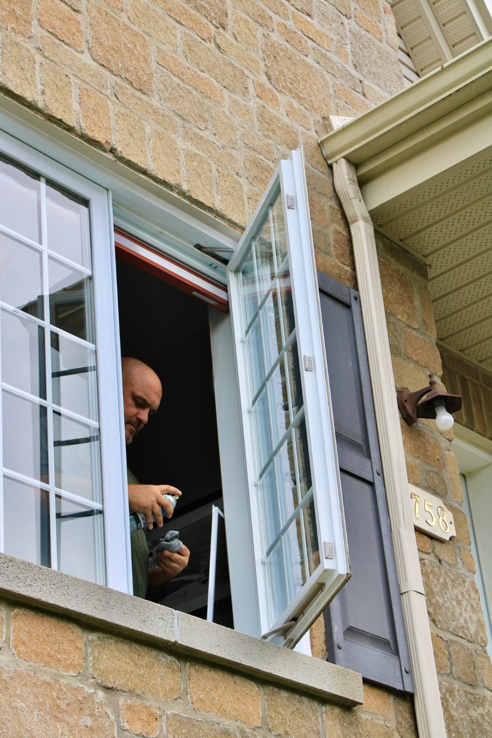 Person looking out an open window with white shutters on a stone house.