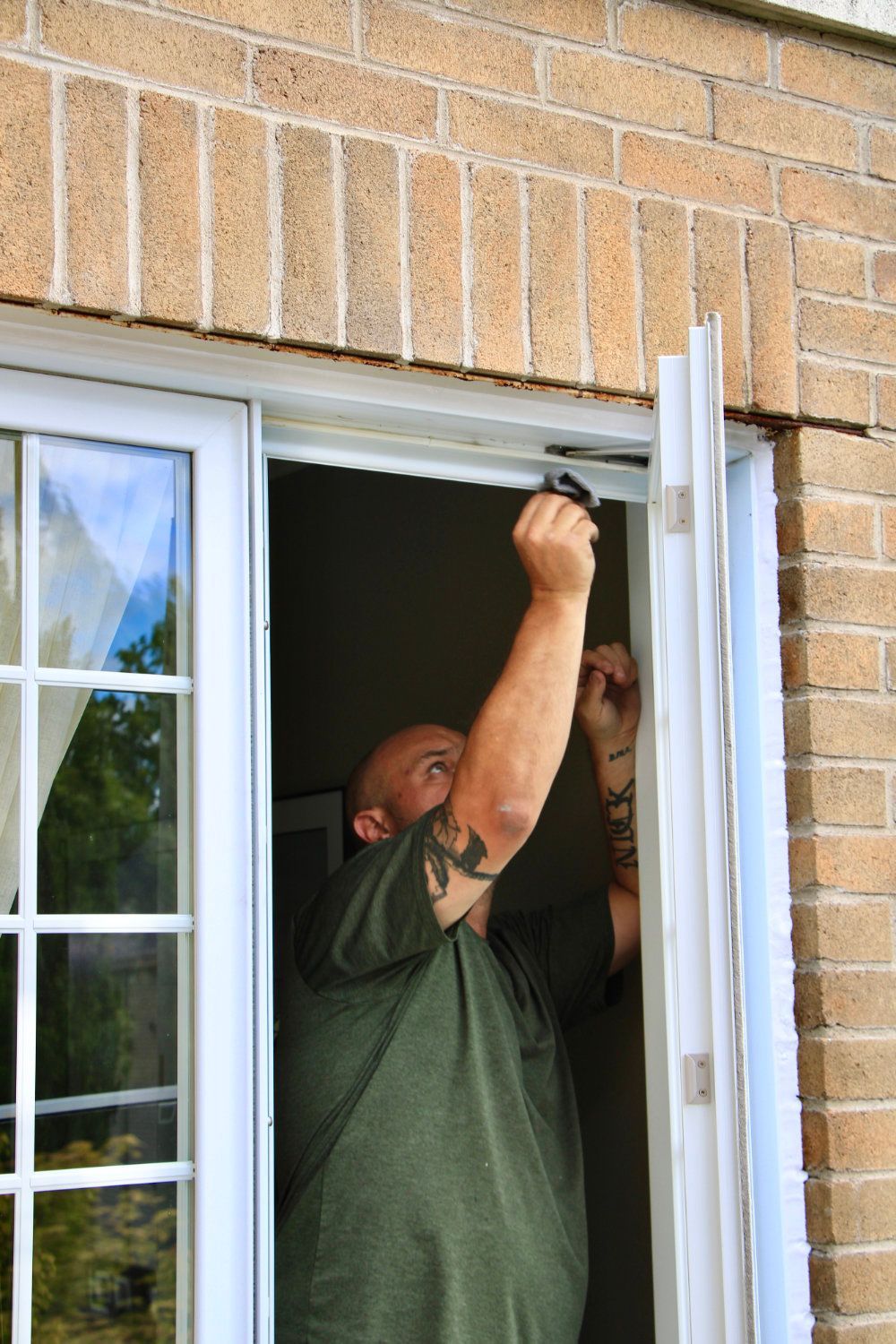 Man in green shirt installing a window frame on a brick house exterior