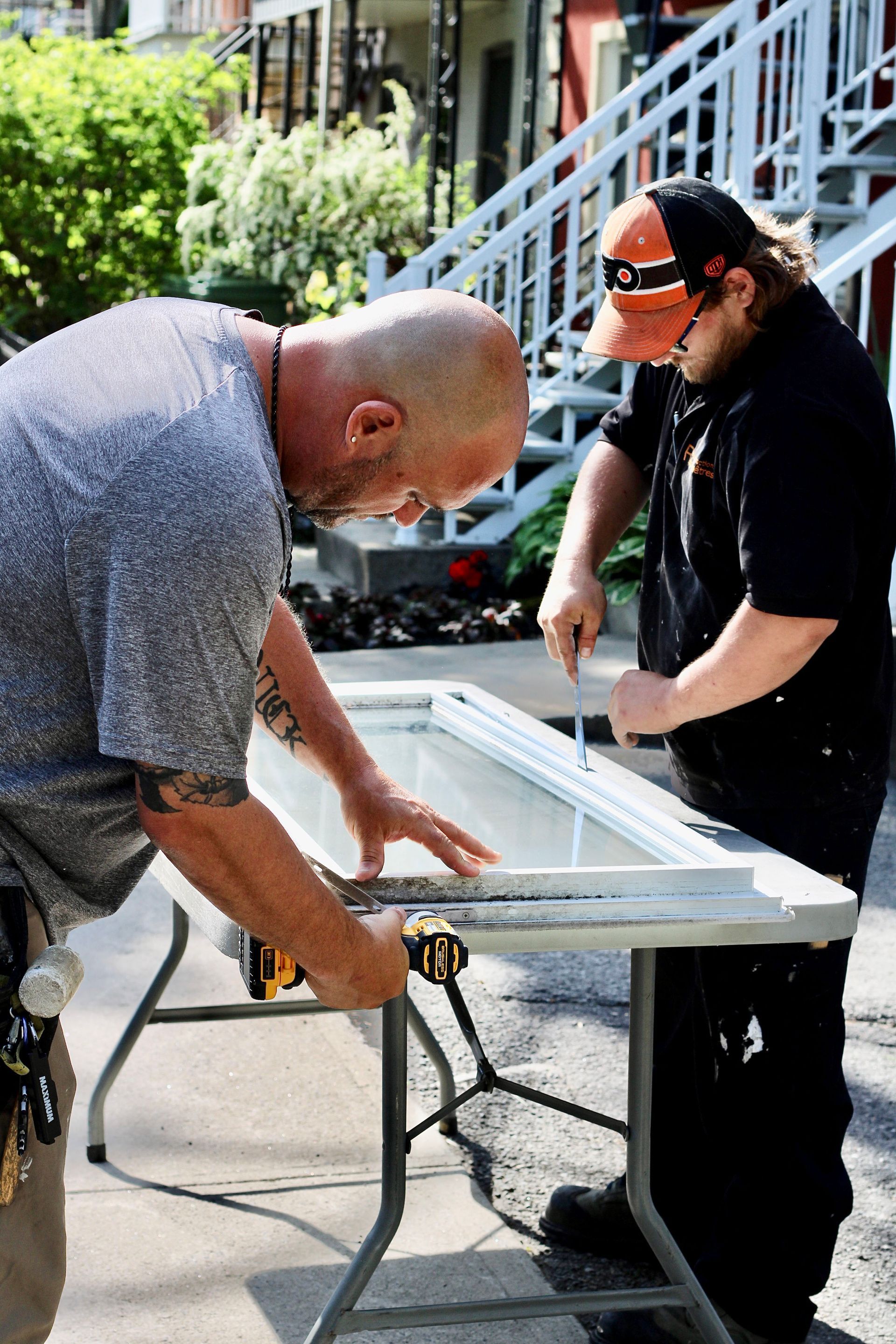 Two workers measuring a white door frame on a folding table outdoors