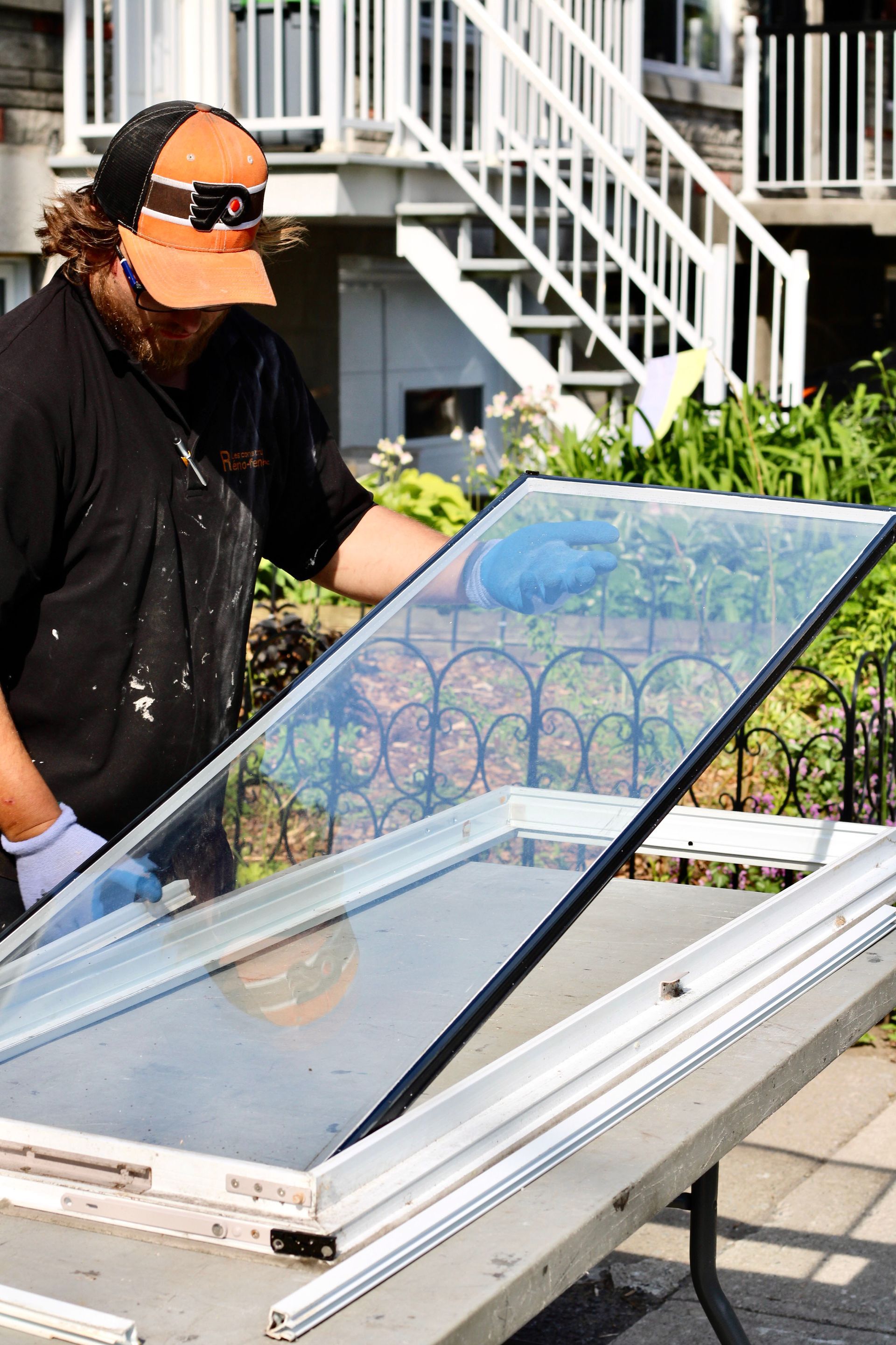 Person inspecting an open rooftop window or skylight beside white stairs and greenery