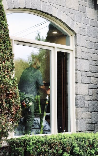 Person seen through a window, painting inside a stone building, with a hedge in front.