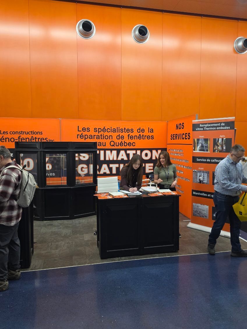 Orange-wall trade booth with posters and a person standing beside a display table in an indoor hall