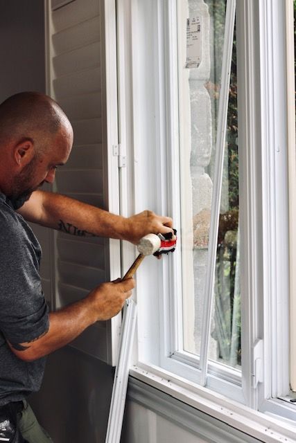 Man caulking the edge of a white window frame with a caulking gun.