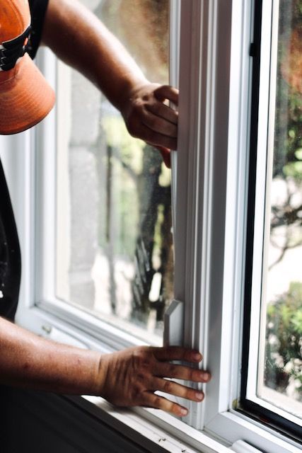 Hands opening a white-framed window beside an orange shirt sleeve