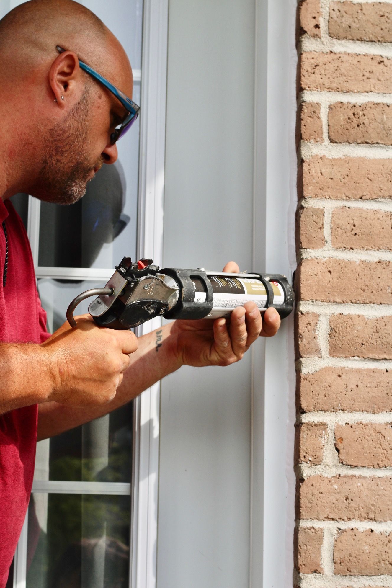 Person applying caulk to a window frame beside a brick wall