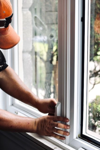 Person installing a silver window latch on a white-framed window.