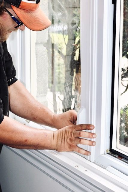 Worker installing a white window frame, adjusting the sill with both hands.