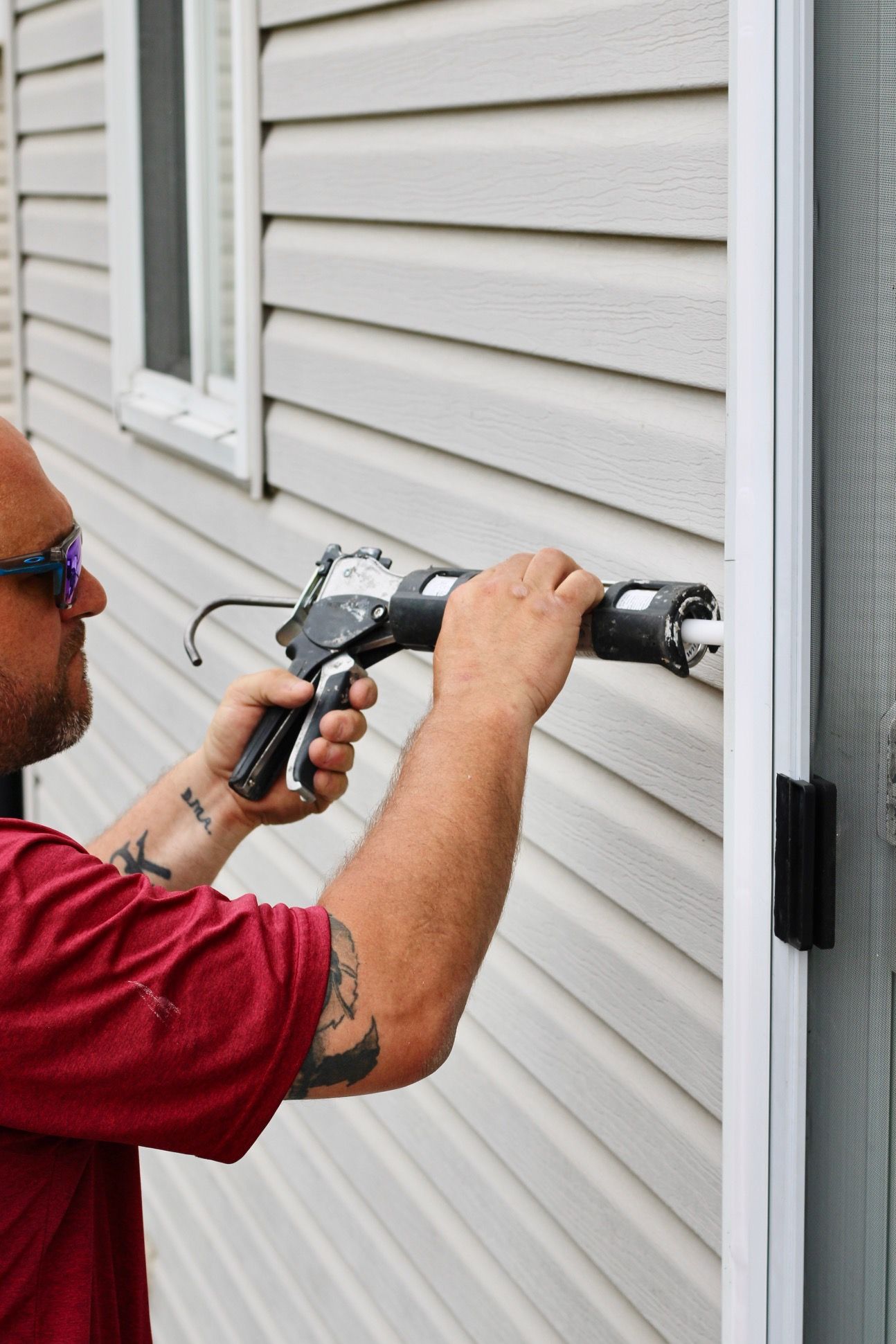 Worker using a power drill to install siding on a house exterior