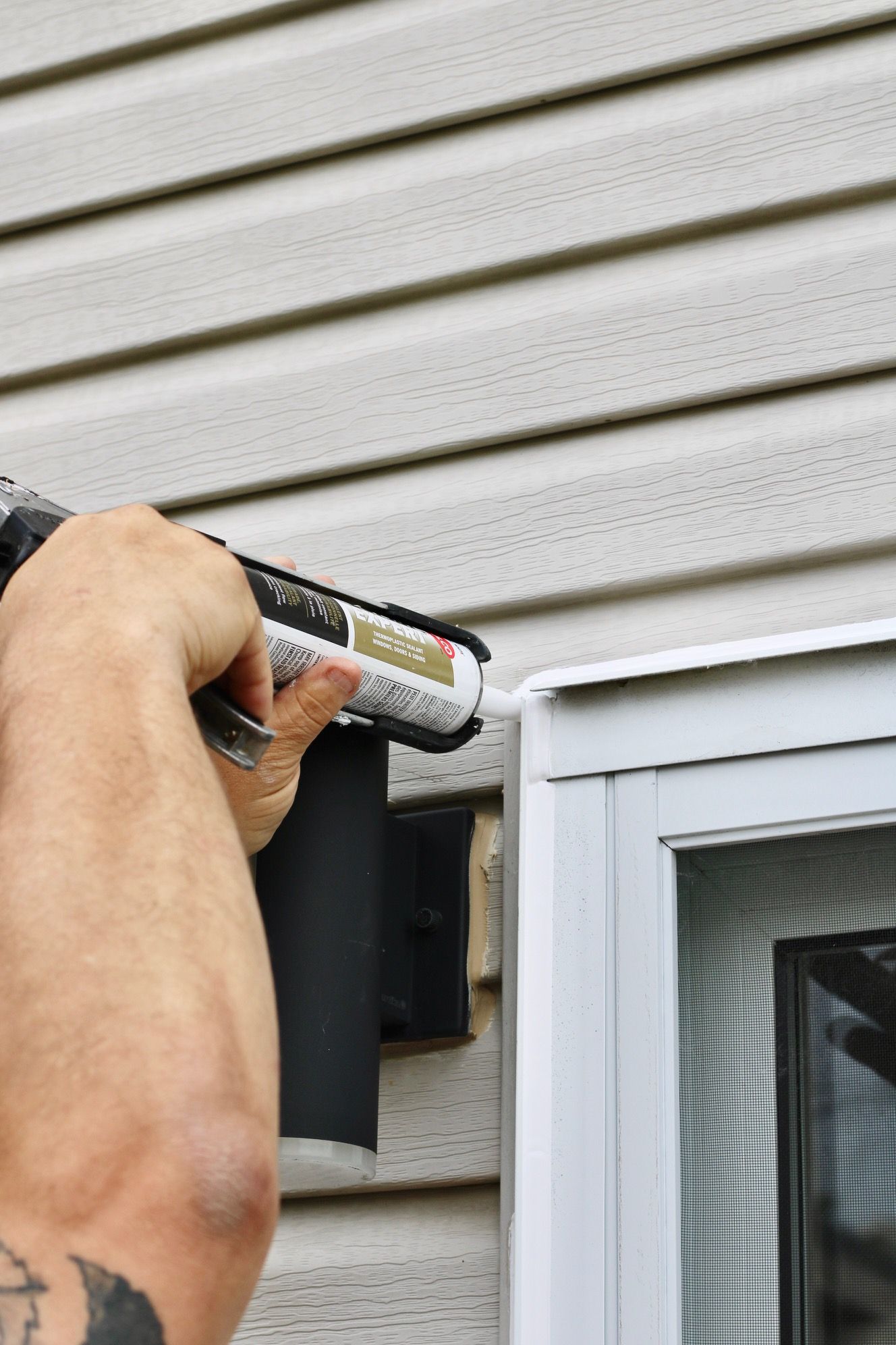 Hand applying caulk along white house siding next to a window frame
