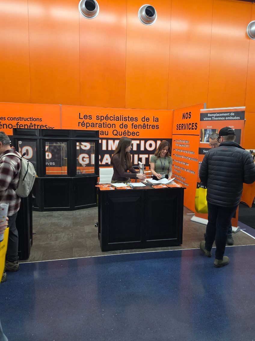 Orange-walled lobby with a black display table, posters, and a few people standing and walking nearby
