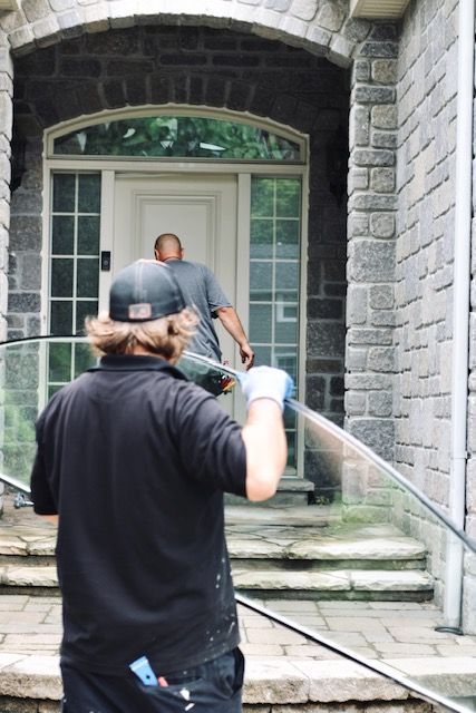 Person in black shirt filming a person at a stone house entrance with steps and a glass door.