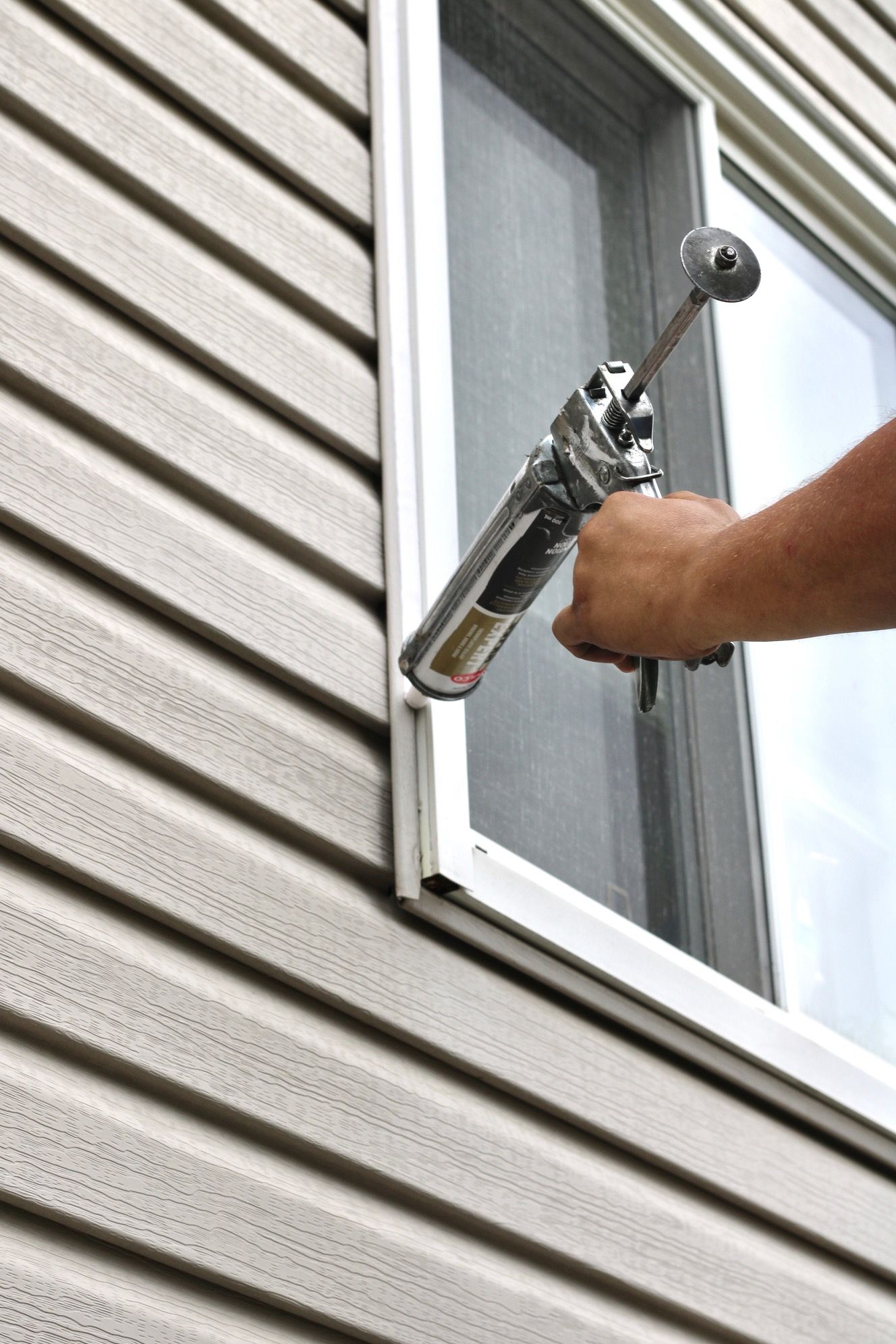 Caulking gun applying sealant to the exterior window frame of a house