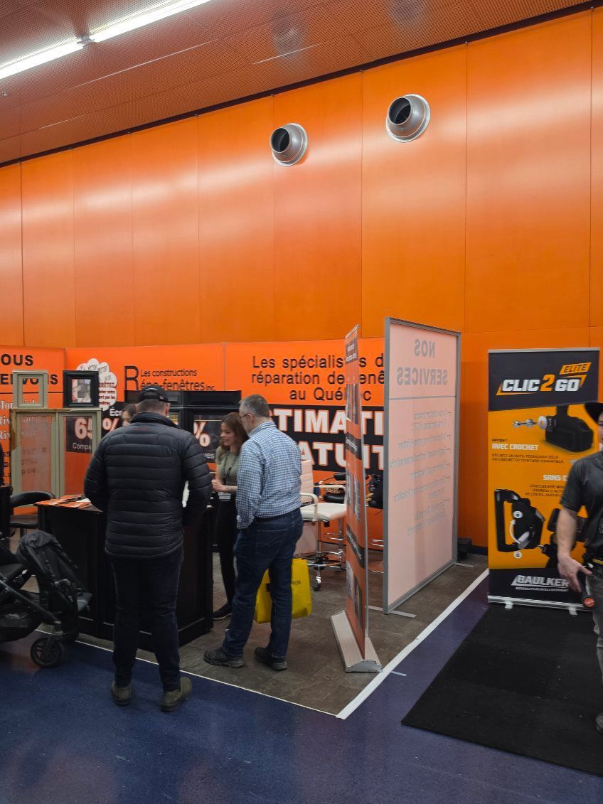 Trade show booth with people gathered around an orange display and a black/orange machine.