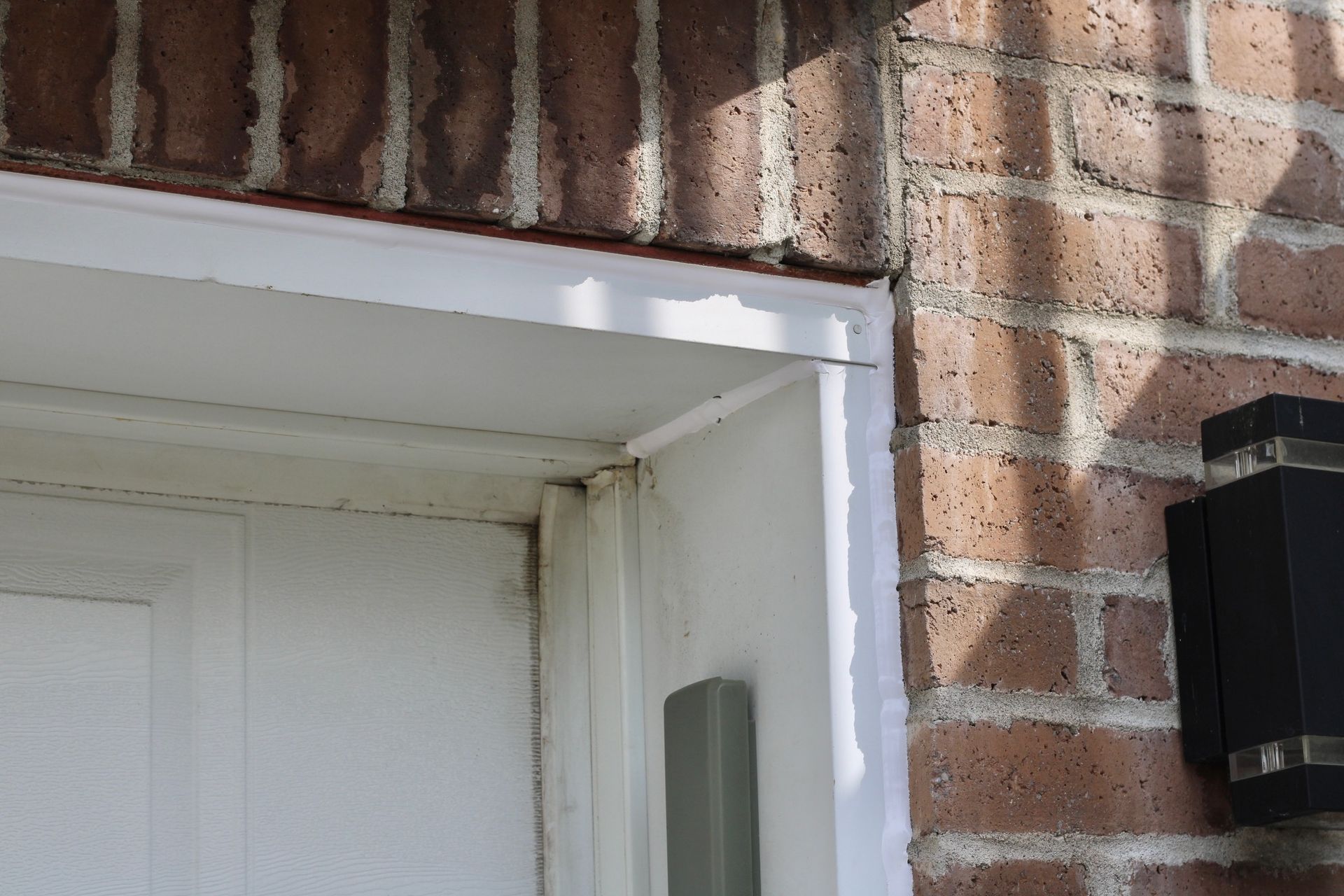 Close-up of a white front door frame with peeling paint on a brick house exterior.