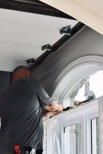 Worker installing a window blind above a white bay window in a room with arched ceiling trim