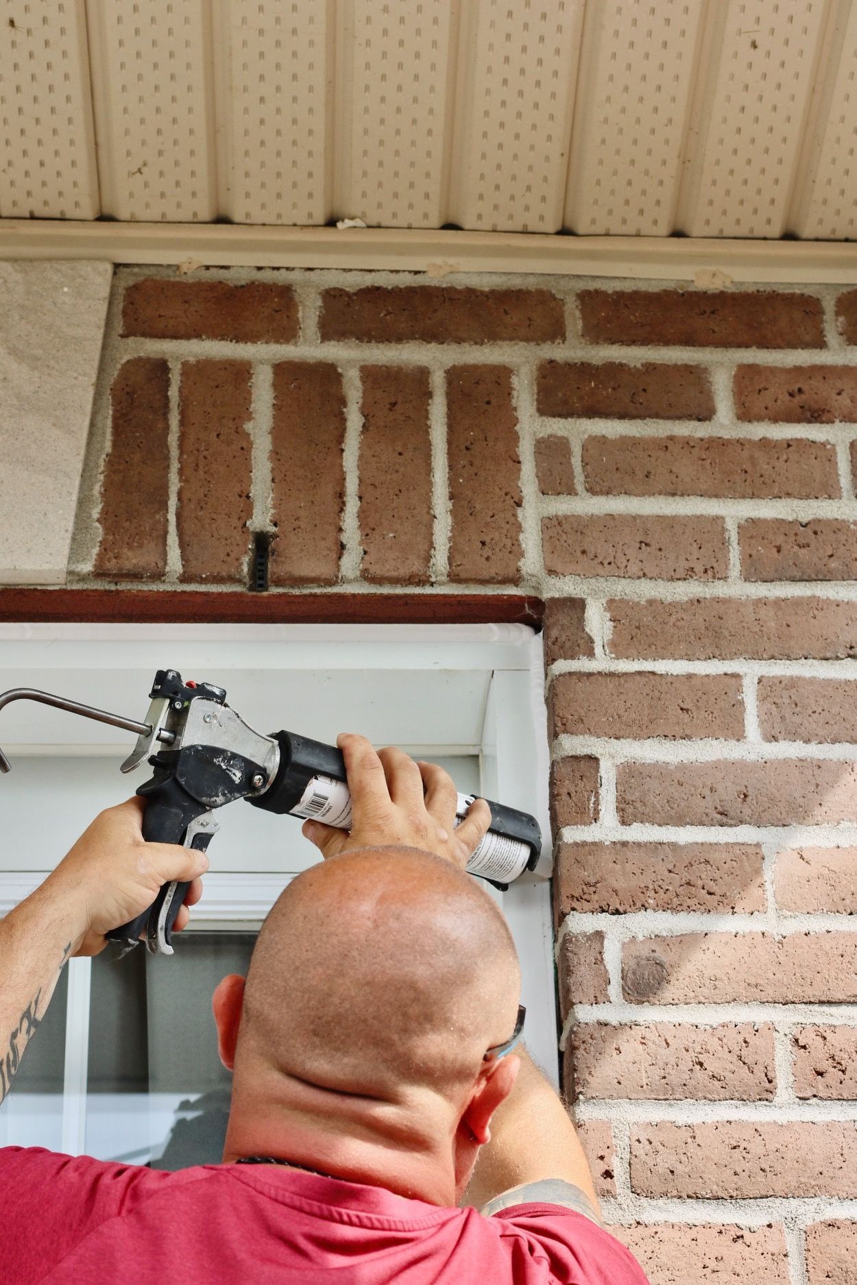 Person caulking around a window under a brick wall and soffit