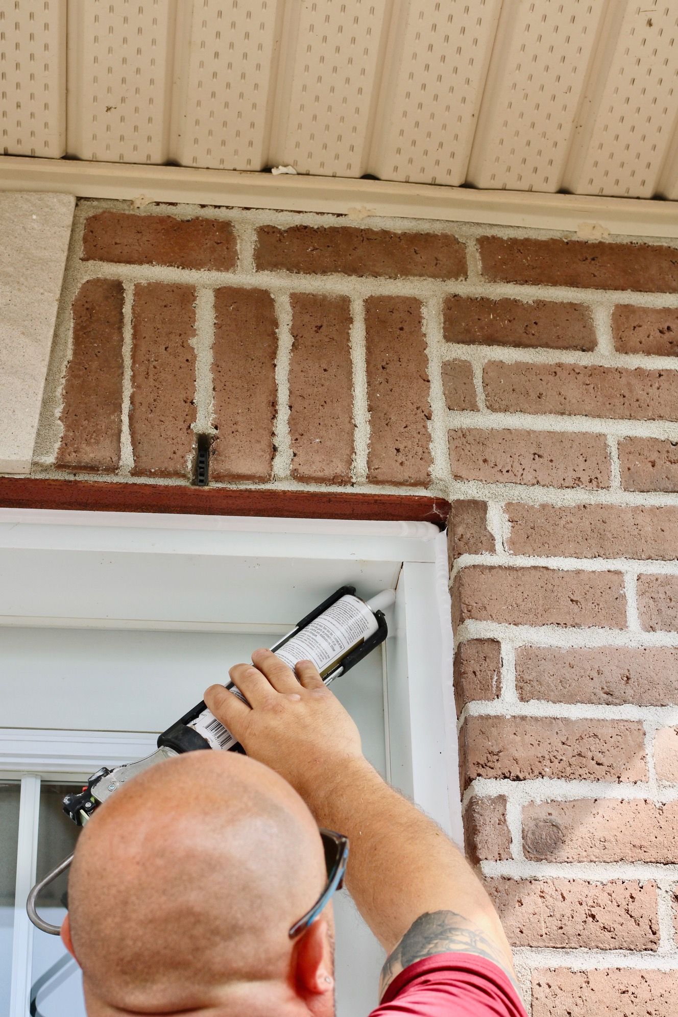 Worker sealing the top of a brick doorway with a caulking gun under a porch ceiling