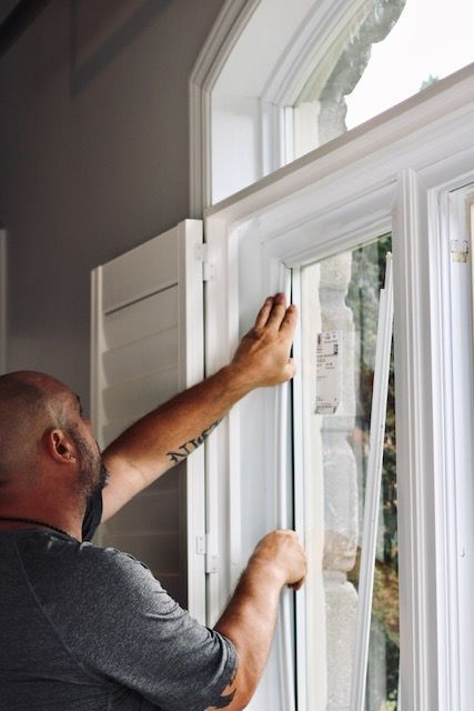 Man installing a white window frame inside a house near an arched window