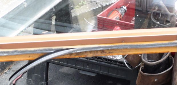 Inside a vehicle, dashboard area with metal tubing, wiring, and a red tool tray visible through the windshield.
