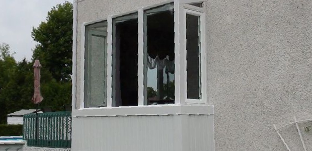 Broken window on a gray house exterior with a white-trimmed bay window.