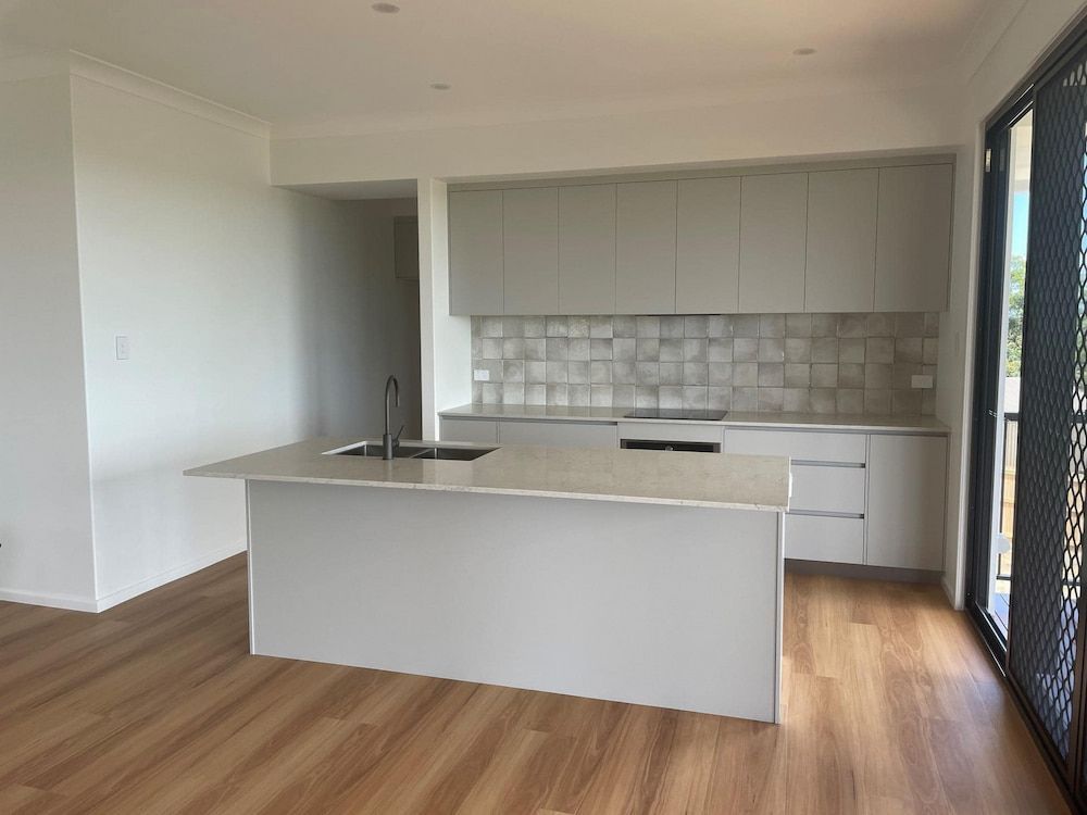 An Empty Kitchen With White Cabinets And A Large Island — Pioneer Cabinets in Paget, QLD