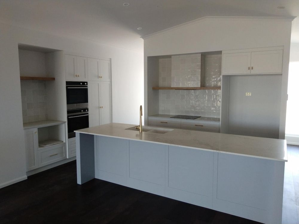 An Empty Kitchen With White Cabinets And A Large Island — Pioneer Cabinets in Paget, QLD