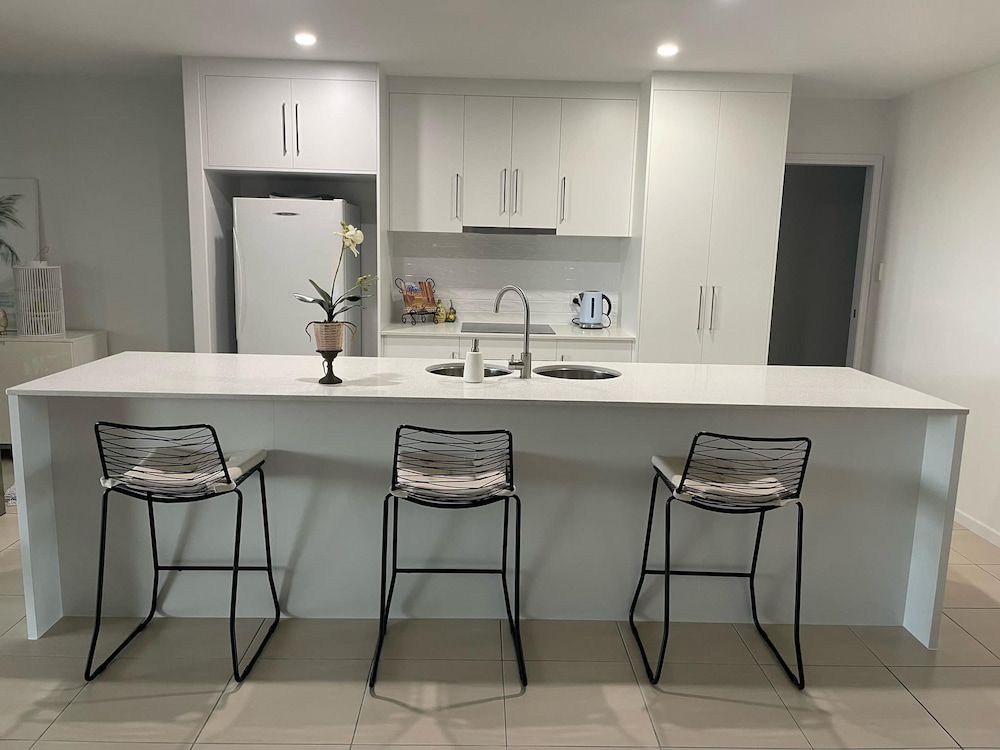 A Kitchen With A Large Island And Three Bar Stools — Pioneer Cabinets in Moranbah, QLD