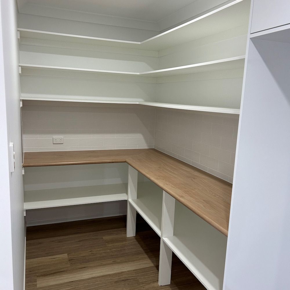 A Walk In Pantry With White Shelves And A Wooden Table — Pioneer Cabinets in Airlie Beach, QLD