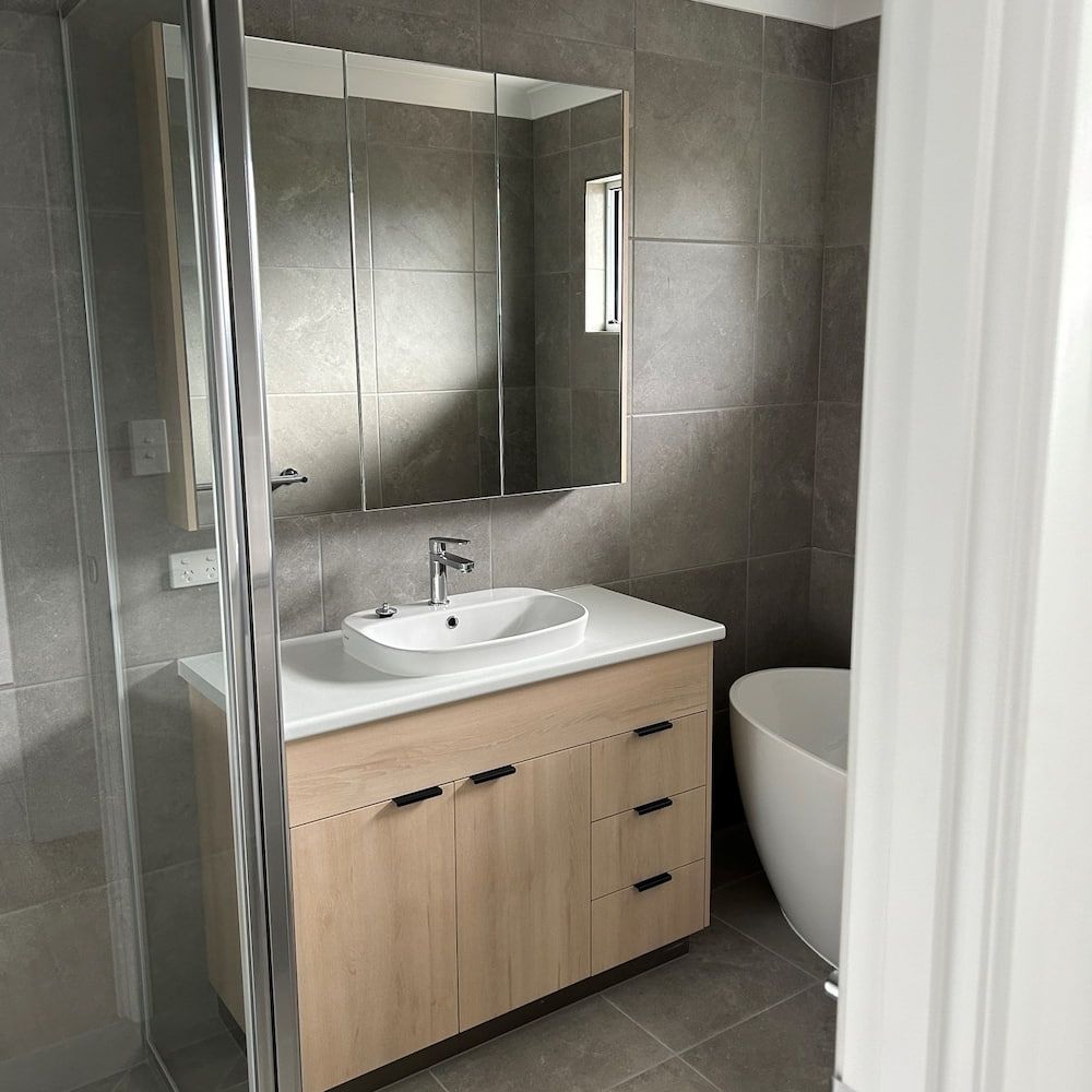 A Bathroom With A Sink, Mirror And Tub — Pioneer Cabinets in Moranbah, QLD