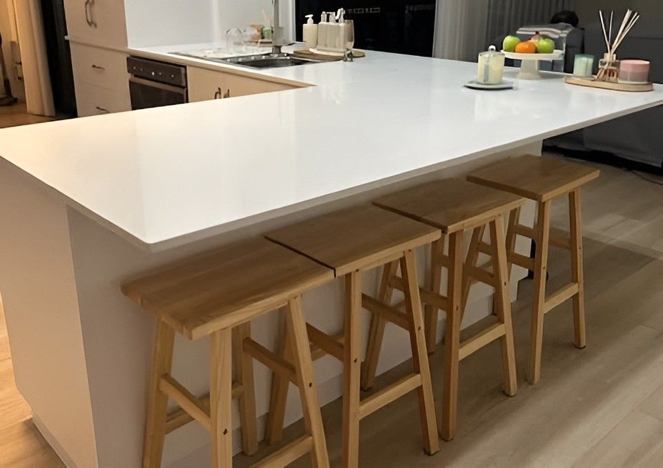 Modern kitchen with a white island and four wooden bar stools, showcasing Kitchen Benchtops Mackay.